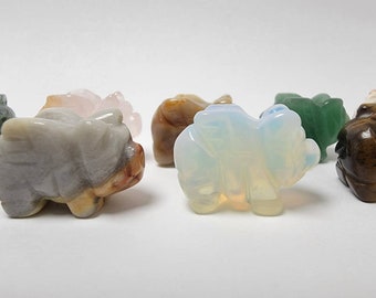 May include: A collection of eight small, carved pig figurines made of various types of stone. The pigs are in different colors, including green, brown, pink, white, and gray.