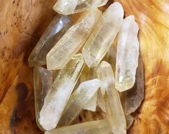 May include: A collection of yellow citrine crystal points in a wooden bowl. The crystals are various sizes and shapes, with some being long and thin, while others are shorter and thicker.