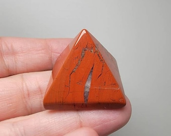 May include: A red jasper pyramid crystal with white and brown veins. The pyramid is smooth and polished.