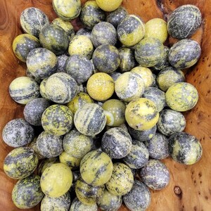 May include: A collection of oval-shaped stones in a wooden bowl. The stones have a mix of yellow and gray-black colors, with a speckled and marbled appearance. The bowl is made of wood with a warm, brown tone.
