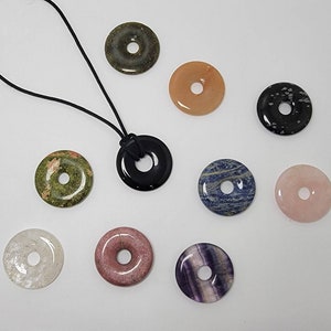 May include: A set of ten stone donut pendants, each with a different color and pattern. The pendants are strung on a black cord necklace. The stones include green, black, pink, white, blue, and brown.