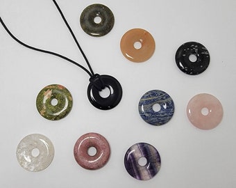 May include: A set of ten stone donut pendants, each with a different color and pattern. The pendants are strung on a black cord necklace. The stones include green, black, pink, white, blue, and brown.