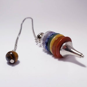 May include: A silver chain with a silver and gemstone pendulum. The pendulum has a pointed tip and is made up of seven stacked, round gemstones in various colors, including red, orange, yellow, green, blue, and purple.