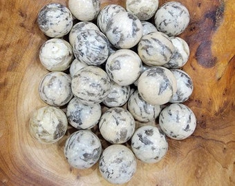 May include: A collection of 20 smooth, white and gray, polished, round, natural stone spheres. The spheres are arranged in a pile on a wooden surface.