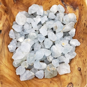 May include: A bowl filled with light blue celestite crystal chips. The crystals are rough and have a natural, unpolished look.