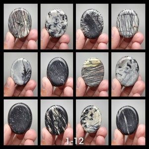 May include: Twelve smooth, oval-shaped stones with black and white patterns. The stones are arranged in a grid of four rows and three columns.