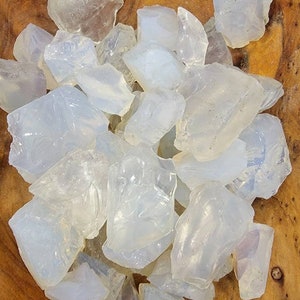 May include: A collection of translucent white opalite stones in various shapes and sizes. The stones are arranged in a wooden bowl.