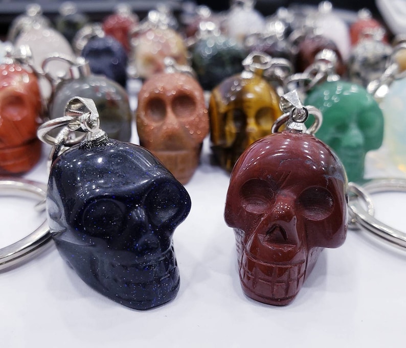 May include: Two skull-shaped keychains made of polished stone. One is dark blue with silver flecks and the other is a deep red. Both have silver key rings.