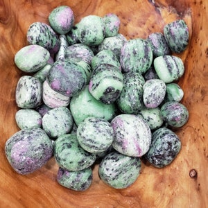 May include: A collection of green, black, and pink tumbled stones. The stones are smooth and polished, and they have a variety of patterns and textures.