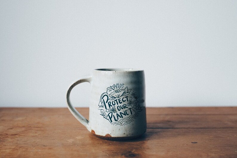 May include: White ceramic mug with a black and white illustration of flowers and the text "Protect Our Planet".