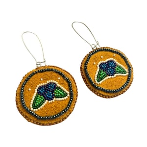 Può includere: Un paio di orecchini rotondi con sfondo color senape. Ogni orecchino presenta un disegno di perline di bacche blu e verdi con accenti bianchi. Gli orecchini hanno un bordo di perline scure e fili per le orecchie color argento.