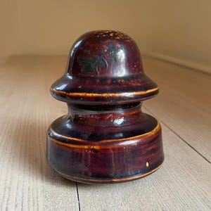 May include: A brown ceramic insulator with a dark brown glaze and a yellow rim. The insulator has a rounded top and a wide base.