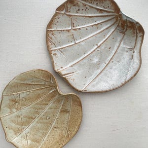 May include: Two ceramic plates with a leaf design. The plates are white with brown accents and have a textured surface.