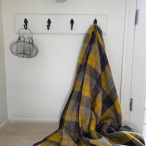 May include: A yellow and gray plaid throw blanket with fringe hanging on a white wall hook. The blanket is draped over the hook and falls to the floor.