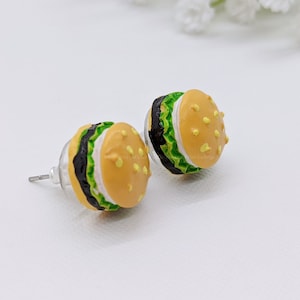 May include: A pair of yellow, green, and black hamburger earrings. The earrings are made of polymer clay and have a realistic look.