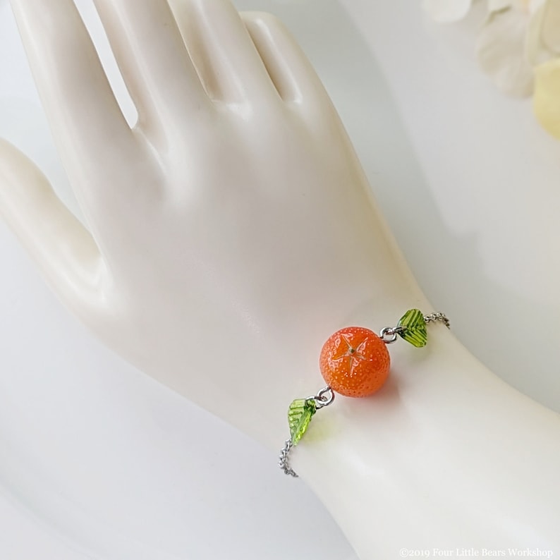 May include: A silver chain bracelet with a bright orange fruit charm and green leaf charms.
