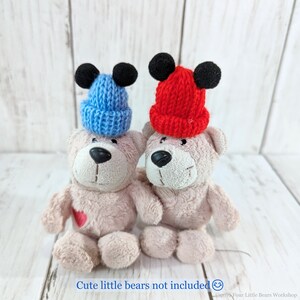 Pu&ograve; includere: Due cappelli di lana con le orecchie nere. Un cappello &egrave; rosso e l'altro &egrave; blu. I cappelli sono posizionati sopra due orsacchiotti.
