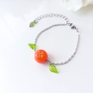 May include: A silver chain bracelet with a bright orange fruit charm and two green leaf charms.