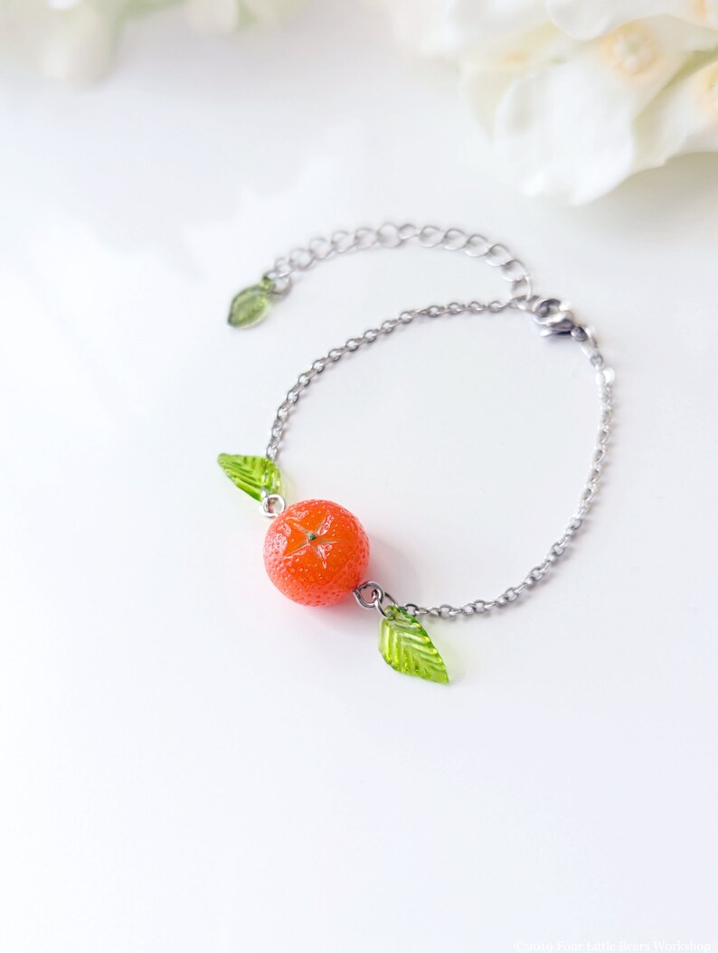 May include: A silver chain bracelet with a bright orange fruit charm and two green leaf charms.