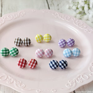 May include: Assortment of colorful gingham fabric covered buttons displayed on a pink plate. The buttons are in pairs and come in the colors green, brown, yellow, pink, purple, blue, and red.
