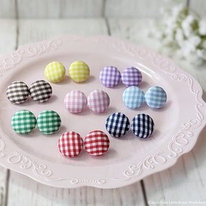 May include: Assortment of 10 gingham fabric covered buttons in various colors, including red, blue, green, yellow, pink, and brown. The buttons are arranged in pairs on a pink plate with a decorative border.