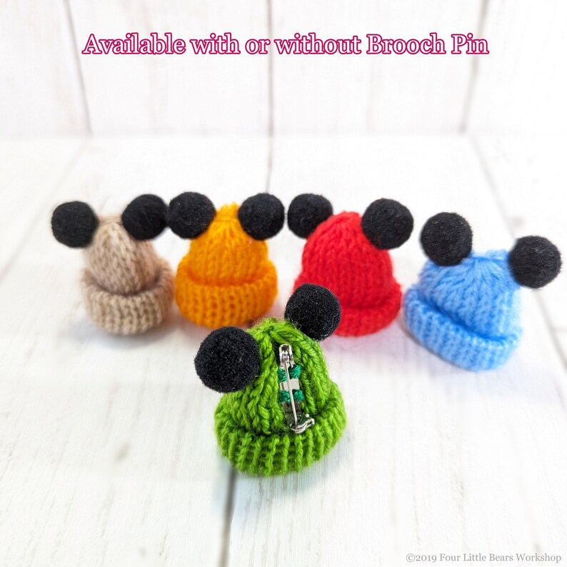 Pu&ograve; includere: Cinque cappellini in miniatura di lana con pompon neri in cima. I cappellini sono di vari colori: beige, arancione, rosso, blu e verde. Un cappellino ha una spilla di sicurezza attaccata.