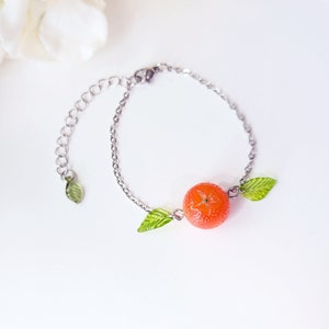 May include: A silver chain bracelet with a bright orange fruit charm and two green leaf charms.