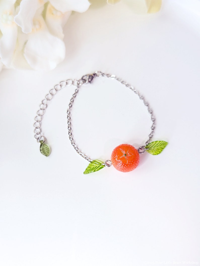 May include: A silver chain bracelet with a bright orange fruit charm and two green leaf charms.