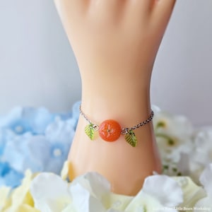 May include: A silver chain bracelet with a small orange slice charm and two green leaf charms.