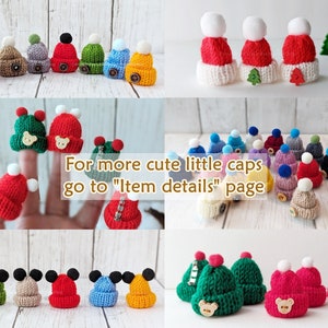 Pu&ograve; includere: Assortimento di cappelli di lana colorati con pon pon. I cappelli sono piccoli e presentano vari disegni, tra cui un orso, un albero di Natale e una testa di Topolino. Il testo "Per altri cappelli piccoli e carini, visita la pagina "Dettagli dell'articolo" &egrave; visualizzato nell'immagine.