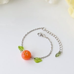 May include: A silver chain bracelet with a small orange charm and green leaf charms.