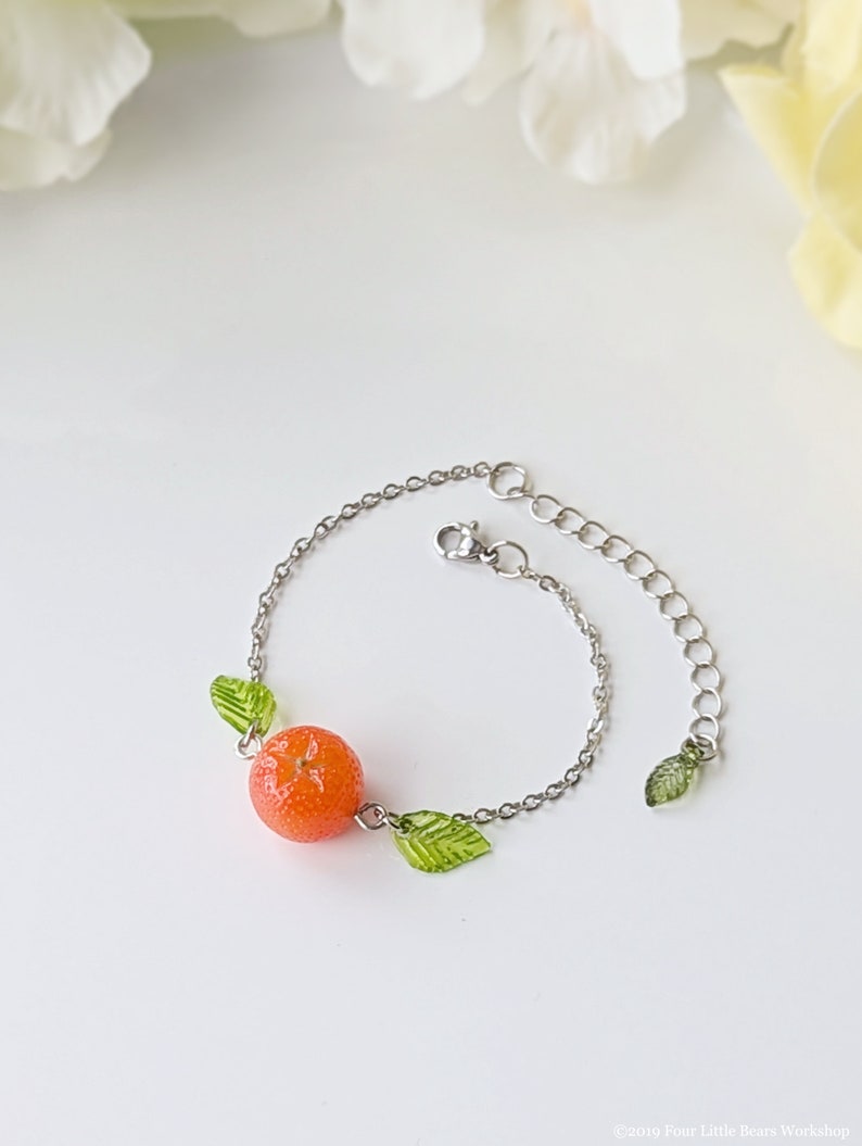 May include: A silver chain bracelet with a small orange charm and green leaf charms.