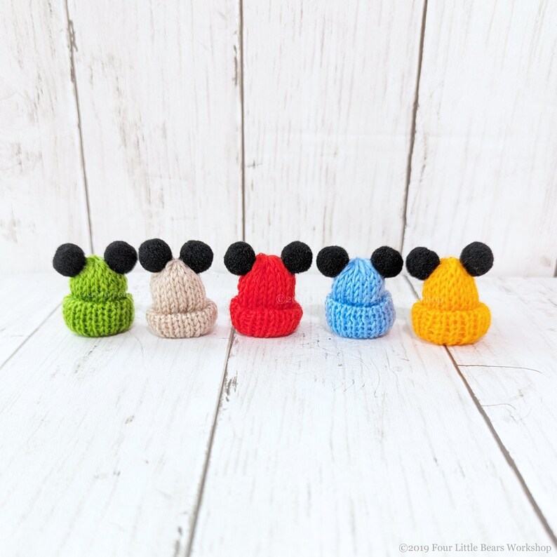 Pu&ograve; includere: Cinque cappellini in miniatura di lana con pompon neri in cima. I cappellini sono di diversi colori: verde, beige, rosso, blu e giallo.