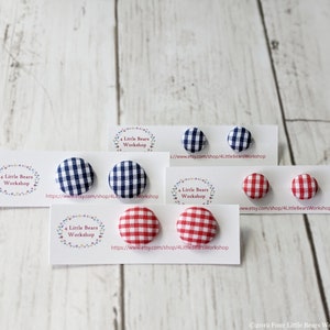 May include: Four pairs of fabric covered button earrings. Two pairs are red and white gingham and two pairs are blue and white gingham. The earrings are displayed on white cards with the text "4 Little Bears Workshop" and a website address.