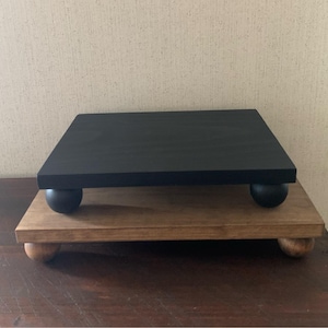 May include: A two-tiered wooden display stand with black painted top and natural wood base. Both tiers have round wooden feet.