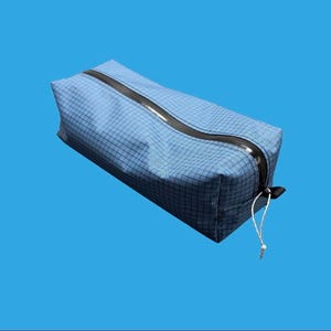 Peut inclure: Une trousse rectangulaire bleue avec un motif &agrave; grille subtil sur toute sa surface. Le sac comprend une fermeture &eacute;clair noire incurv&eacute;e sur le dessus, accompagn&eacute;e d'une fine tirette en cordon blanc fix&eacute;e au curseur pour une ouverture facile.