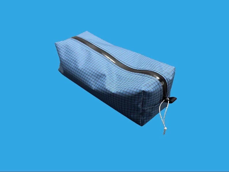 Peut inclure: Une trousse rectangulaire bleue avec un motif &agrave; grille subtil sur toute sa surface. Le sac comprend une fermeture &eacute;clair noire incurv&eacute;e sur le dessus, accompagn&eacute;e d'une fine tirette en cordon blanc fix&eacute;e au curseur pour une ouverture facile.