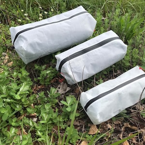 Peut inclure: Trois pochettes de rangement rectangulaires fabriqu&eacute;es dans un mat&eacute;riau blanc translucide, chacune dot&eacute;e d'une fermeture &eacute;clair noire imperm&eacute;able sur le dessus et d'une petite cordelette rouge attach&eacute;e au curseur de la fermeture.
