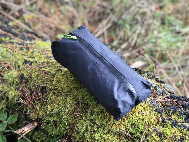 Peut inclure: Une pochette de rangement rectangulaire noire fabriqu&eacute;e dans un tissu l&eacute;ger et froiss&eacute;. La pochette est dot&eacute;e d'une fermeture &eacute;clair noire r&eacute;sistante &agrave; l'eau sur le dessus, agr&eacute;ment&eacute;e d'une tirette vert n&eacute;on vif.