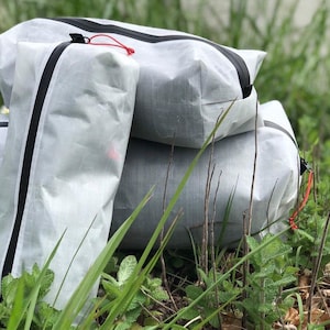 Puede incluir: Tres bolsas de almacenamiento blancas translúcidas con un patrón de cuadrícula, cada una con una cremallera negra impermeable y un pequeño cordón rojo. Las bolsas son rectangulares, de tamaños variados y están apiladas juntas.