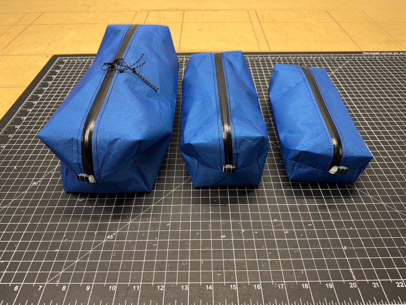 Peut inclure: Trois pochettes de rangement rectangulaires bleues de tailles diff&eacute;rentes, chacune dot&eacute;e d'une fermeture &eacute;clair noire r&eacute;sistante &agrave; l'eau au centre. Les pochettes sont fabriqu&eacute;es dans un mat&eacute;riau lisse et l&eacute;ger avec une forme structur&eacute;e.