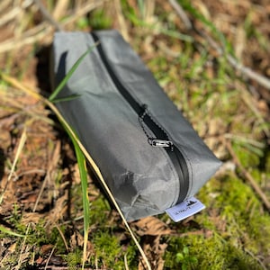 Peut inclure: Une pochette de rangement rectangulaire grise dot&eacute;e d'une fermeture &eacute;clair noire sur le dessus et d'une petite &eacute;tiquette en tissu blanc avec le texte ULTRALITESACKS imprim&eacute; en noir. La pochette est faite d'un mat&eacute;riau synth&eacute;tique tiss&eacute;.