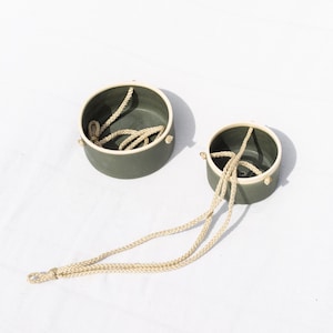 May include: Two green ceramic hanging planters with white rims and a natural rope hanging system.