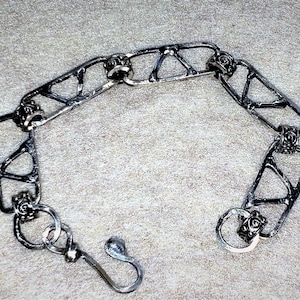 Könnte beinhalten: Ein silbernes Armband mit geometrischem Design und kleinen Dekorationen. Das Armband hat einen Hakenverschluss.