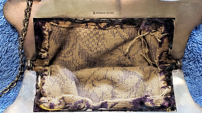 Peut inclure: Un sac &agrave; main argent&eacute; avec une bandouli&egrave;re en cha&icirc;ne et une doublure en tissu. Le sac &agrave; main a une fermeture &agrave; fermoir et les mots "German Silver" sont estampill&eacute;s &agrave; l'int&eacute;rieur.