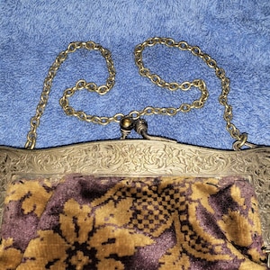 Peut inclure: Un sac &agrave; main vintage en argent et or avec un motif floral et une bandouli&egrave;re en cha&icirc;ne. Le sac est doubl&eacute; d'un tissu &agrave; motifs brun et or.