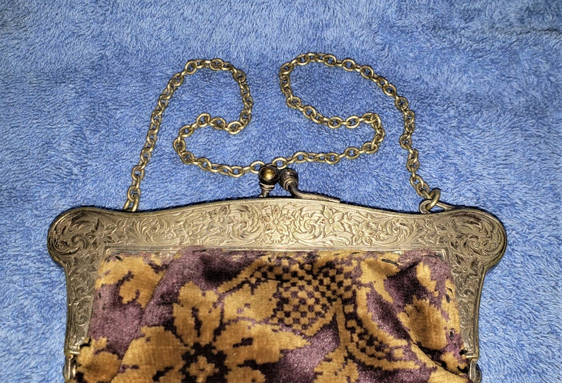 Peut inclure: Un sac &agrave; main vintage en argent et or avec un motif floral et une bandouli&egrave;re en cha&icirc;ne. Le sac est doubl&eacute; d'un tissu &agrave; motifs brun et or.