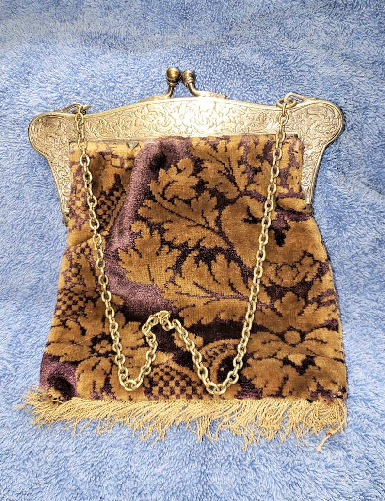 Peut inclure: Un sac &agrave; main vintage en m&eacute;tal dor&eacute; avec un motif floral orn&eacute; et une doublure en velours brun. Le sac &agrave; main a une bandouli&egrave;re en cha&icirc;ne et une bordure en frange.
