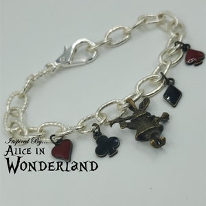 Könnte beinhalten: Silberne Kettenarmband mit Anhängern, inspiriert von Alice im Wunderland. Die Anhänger umfassen ein rotes Herz, ein schwarzes Pik, ein schwarzes Kreuz und eine bronzene Figur des weißen Kaninchens.