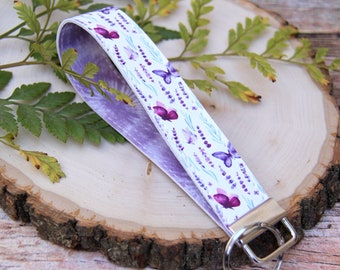 May include: A white and purple key chain with a lavender and butterfly design. The key chain has a silver key ring.